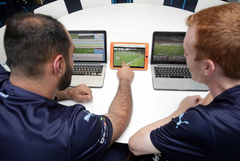 Dois jogadores de futebol assistindo a vídeos de jogos em laptops e tablets