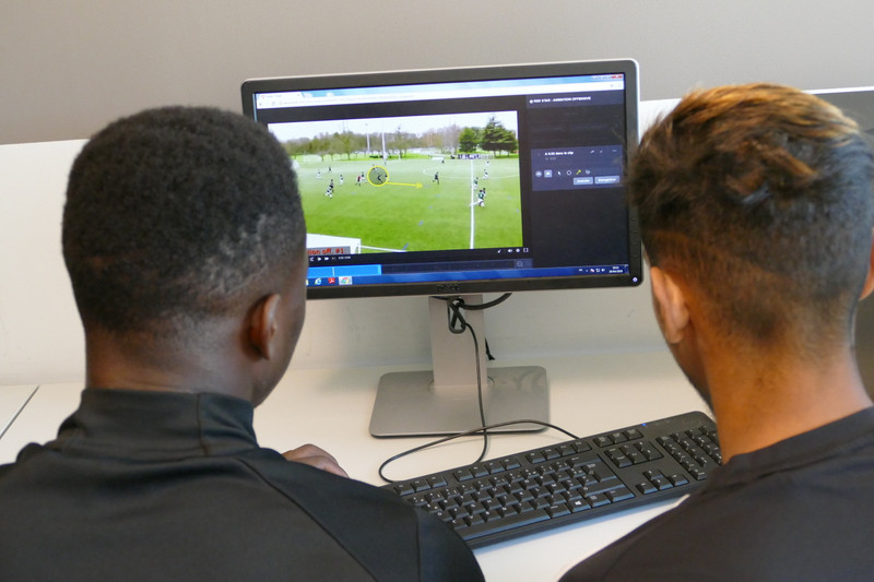 Two players analyse soccer video gameplay at monitor