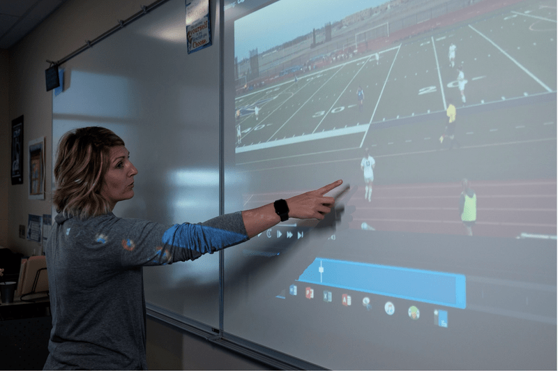 Woman pointing to video projection of soccer match on whiteboard